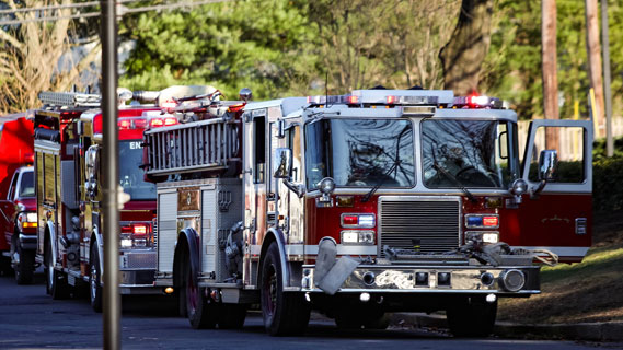 A firetruck with flashing lights driving on a street lined with powerlines and trees